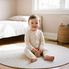 Bebe en pyjama assis sur le tapis rond de sa chambre