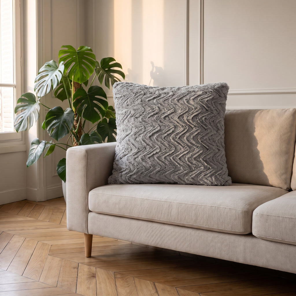 Coussin en coton gris à poil long posé contre l'accoudoir d'un canapé clair