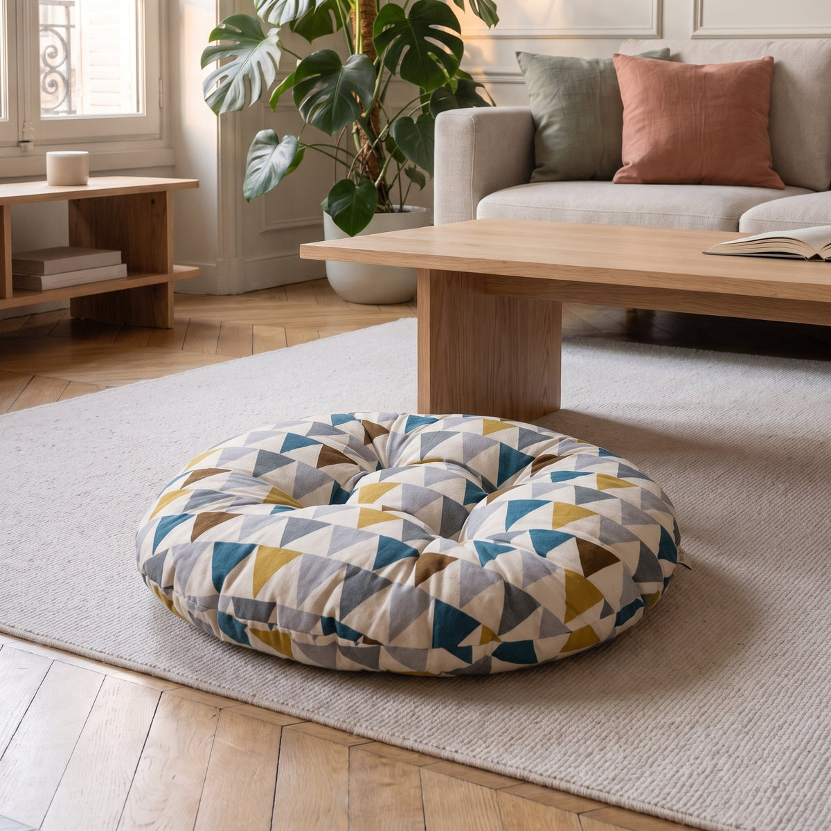 Coussin de sol rond à fanions multicolores posé au sol devant une table basse en bois