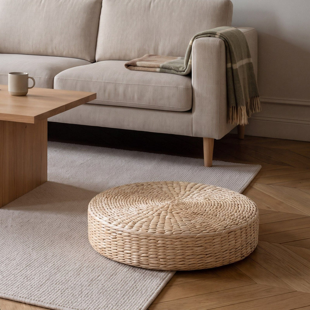 Coussin de sol rond en paille posé sur le parquet, au bord du tapis devant le canapé