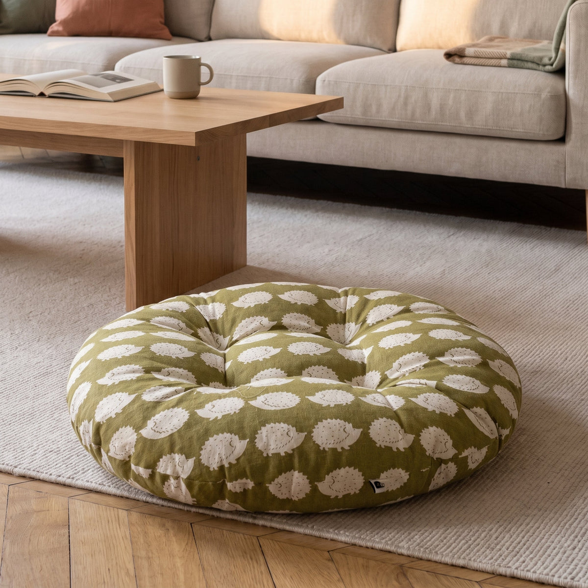 Coussin de sol rond imprimé hérissons blancs sur fond kaki, posé sur un tapis clair
