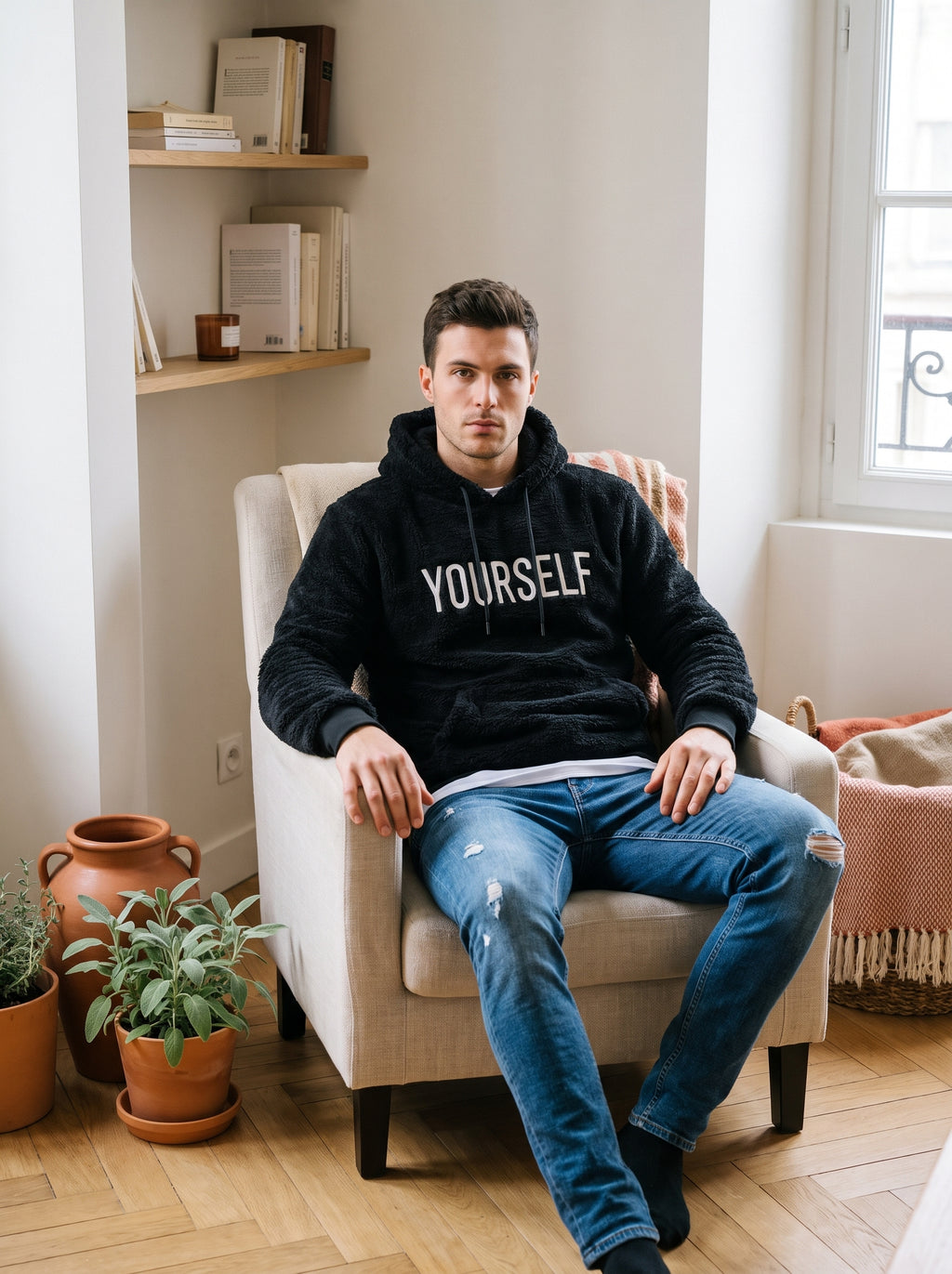 Homme portant le sweat à capuche peluche YOURSELF noir dans un coin lecture