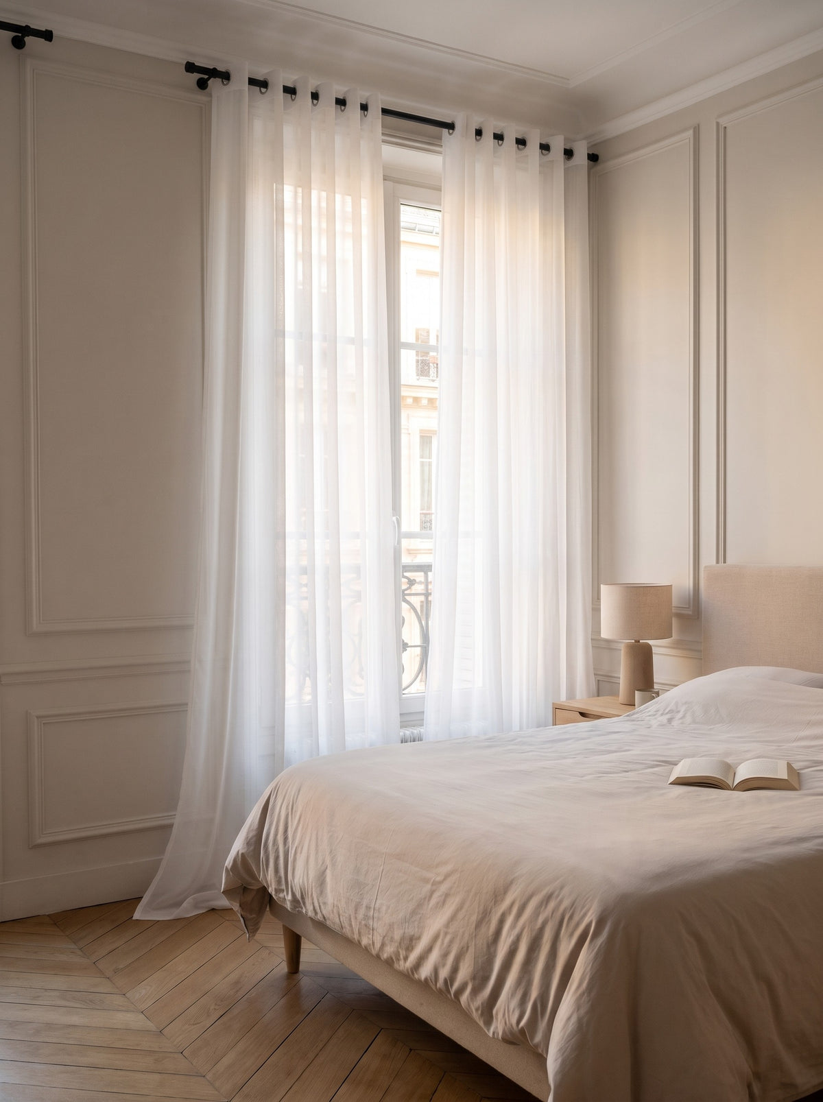Rideau voilage en tulle blanc dans une chambre, les pans descendent de la tringle jusqu'au parquet