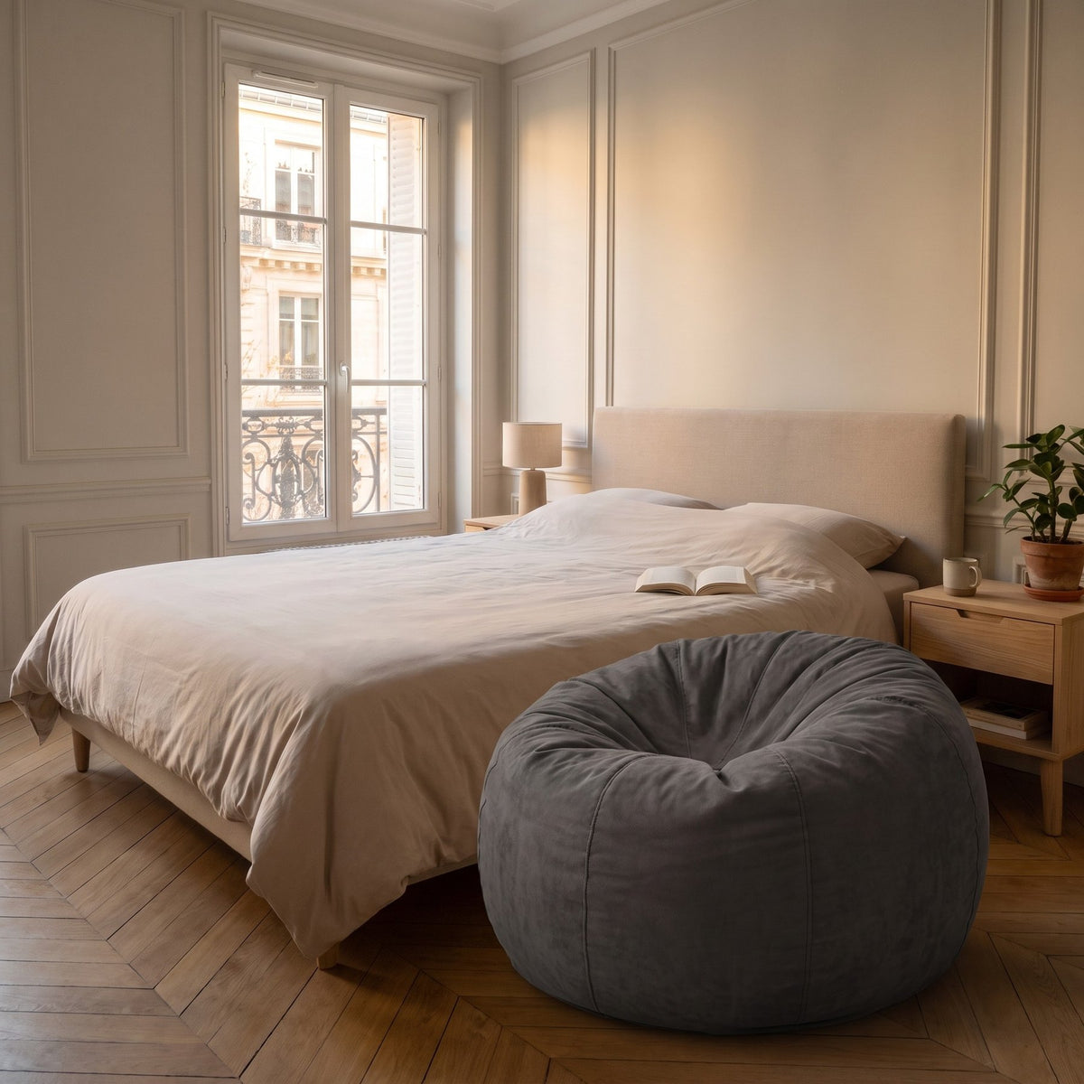 Pouf géant gris foncé en microfibre posé au pied du lit, sur un parquet clair