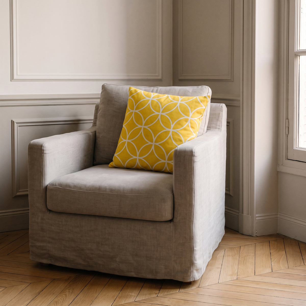 Housse de coussin jaune à cercles entrelacés posée dans l'angle d'un fauteuil en lin clair