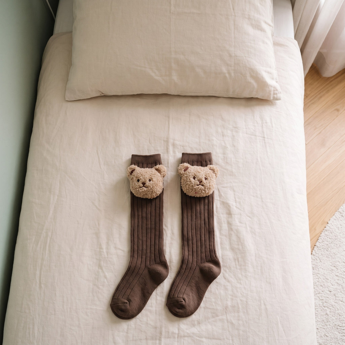 Chaussettes montantes marron pour bébé avec un ourson en peluche, posées sur un lit d'enfant