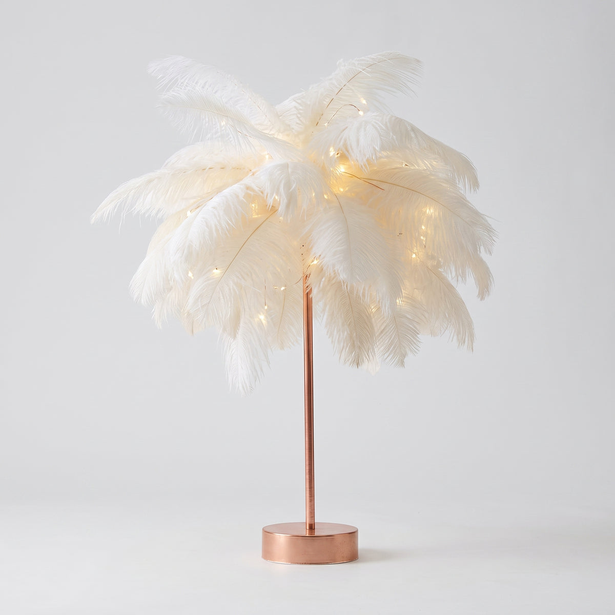 Lampe à plumes blanches entière, socle doré rose, sur fond gris clair