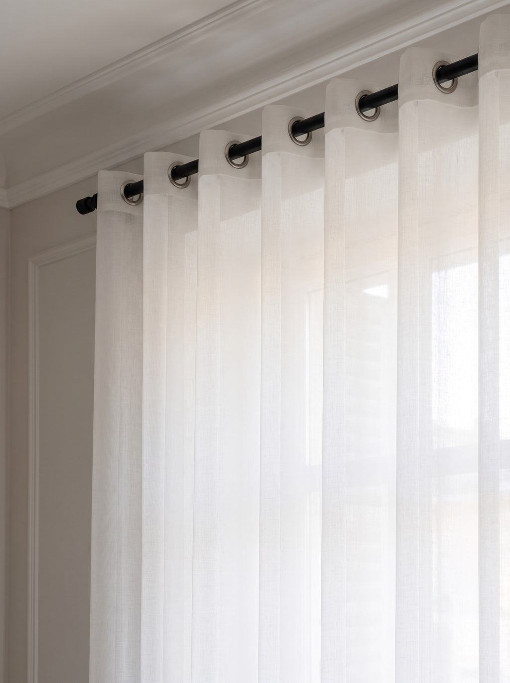 Haut du rideau en tulle blanc enfilé sur une tringle noire par une rangée d'œillets métalliques