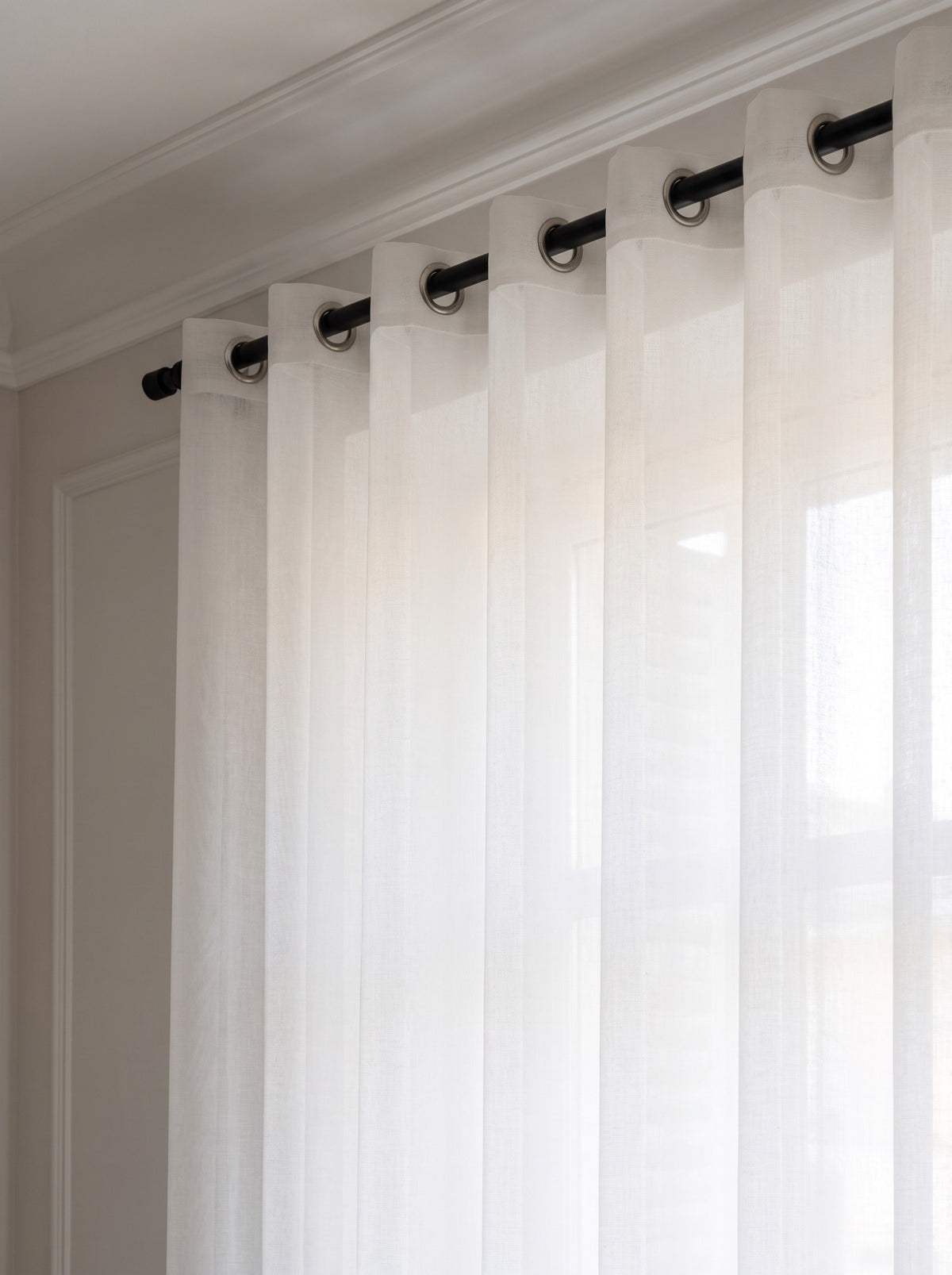Haut du rideau en tulle blanc enfilé sur une tringle noire par une rangée d'œillets métalliques