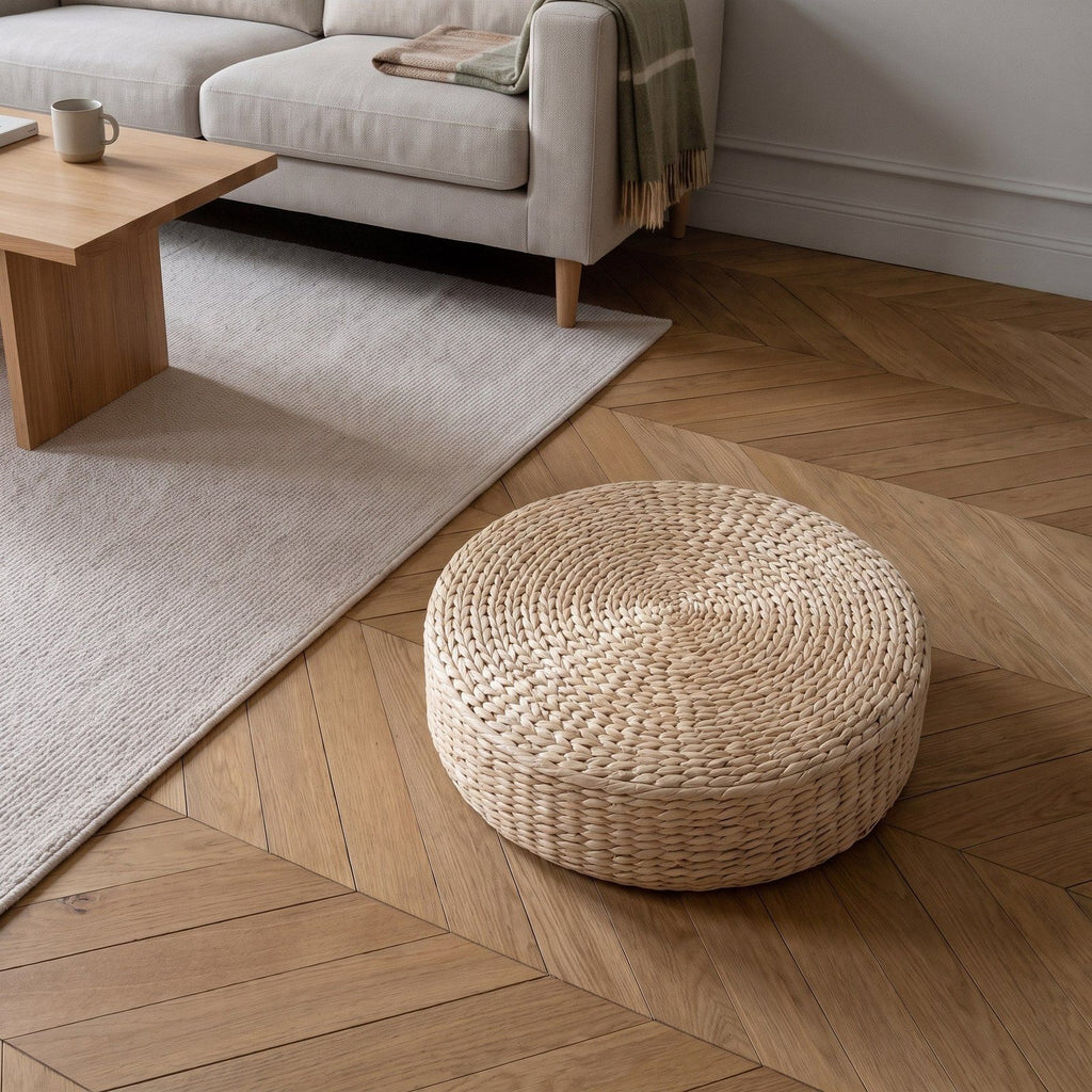 Coussin de sol rond en paille sur un parquet à chevrons, au bord d'un tapis