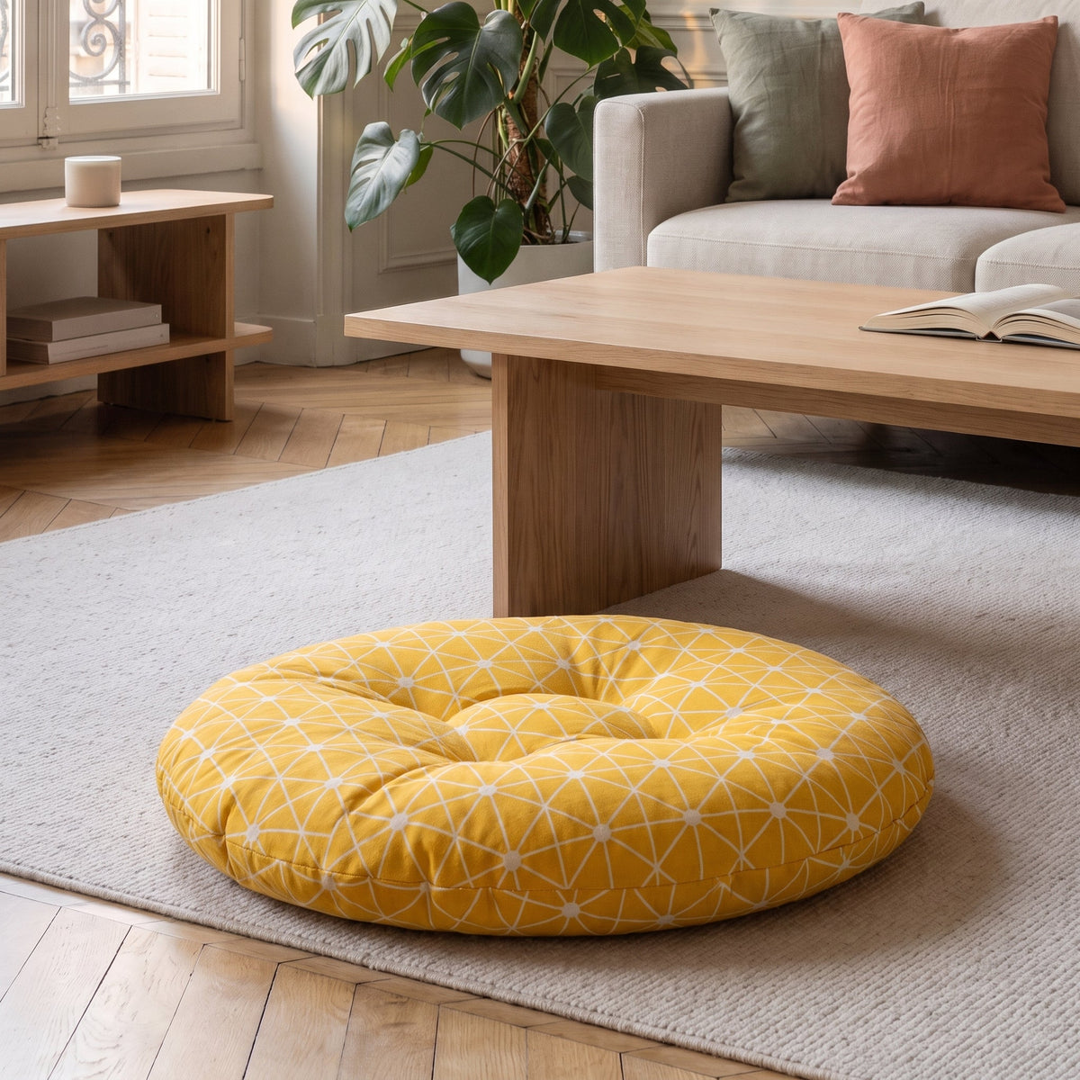 Coussin de sol rond jaune moutarde à étoiles graphiques, posé au sol devant une table basse