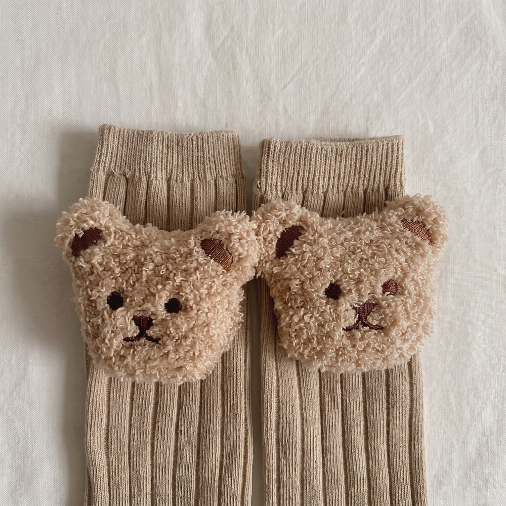 Les deux têtes d'ourson en peluche cousues sur le bord côtelé des chaussettes