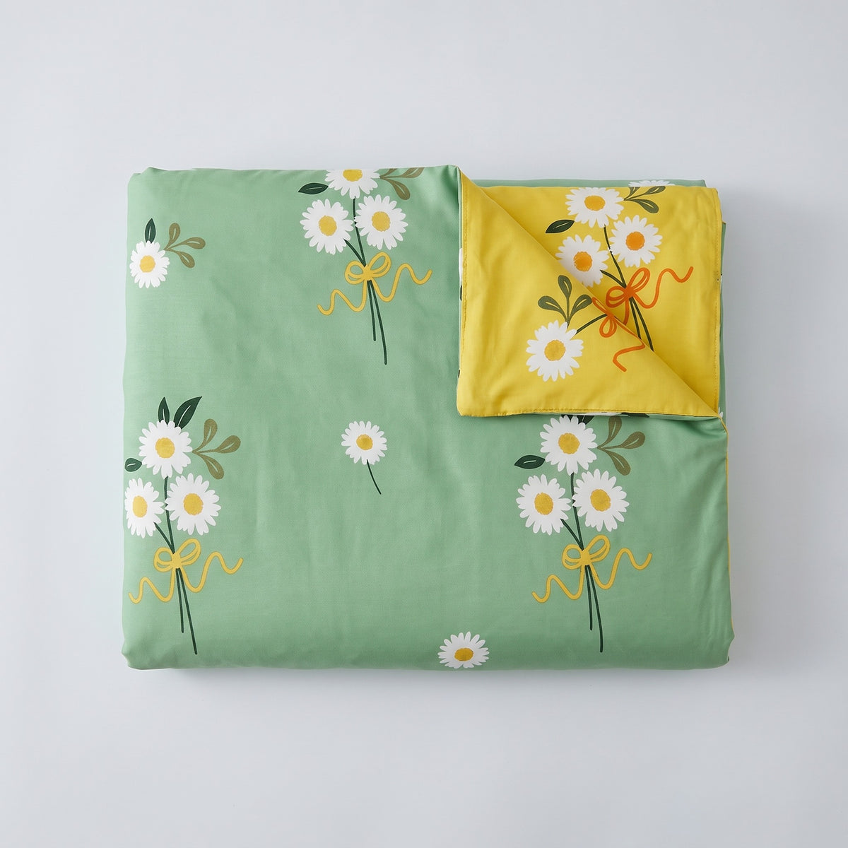 La housse de couette pliée, sa face verte à pâquerettes et sa face jaune au revers