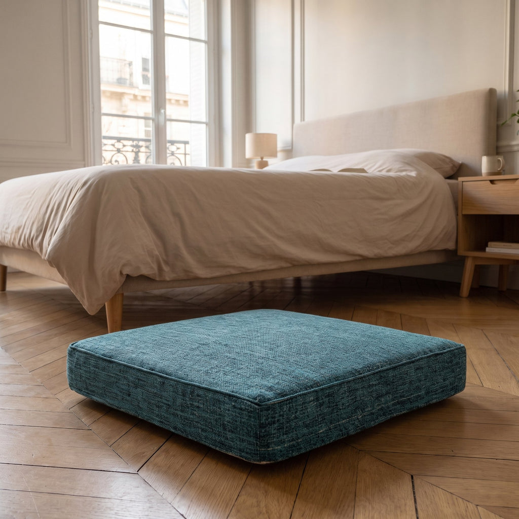 Coussin de sol vert canard posé au pied d'un lit