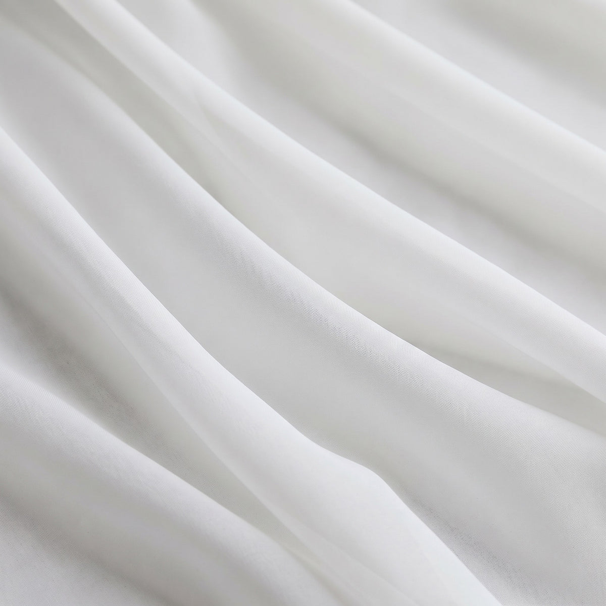 Gros plan sur le tulle blanc drapé en plis souples, la trame fine du voile est visible
