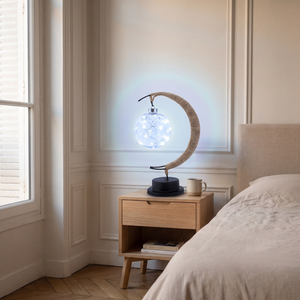 Lampe croissant de lune allumée en blanc froid bleuté, halo pâle sur le mur.