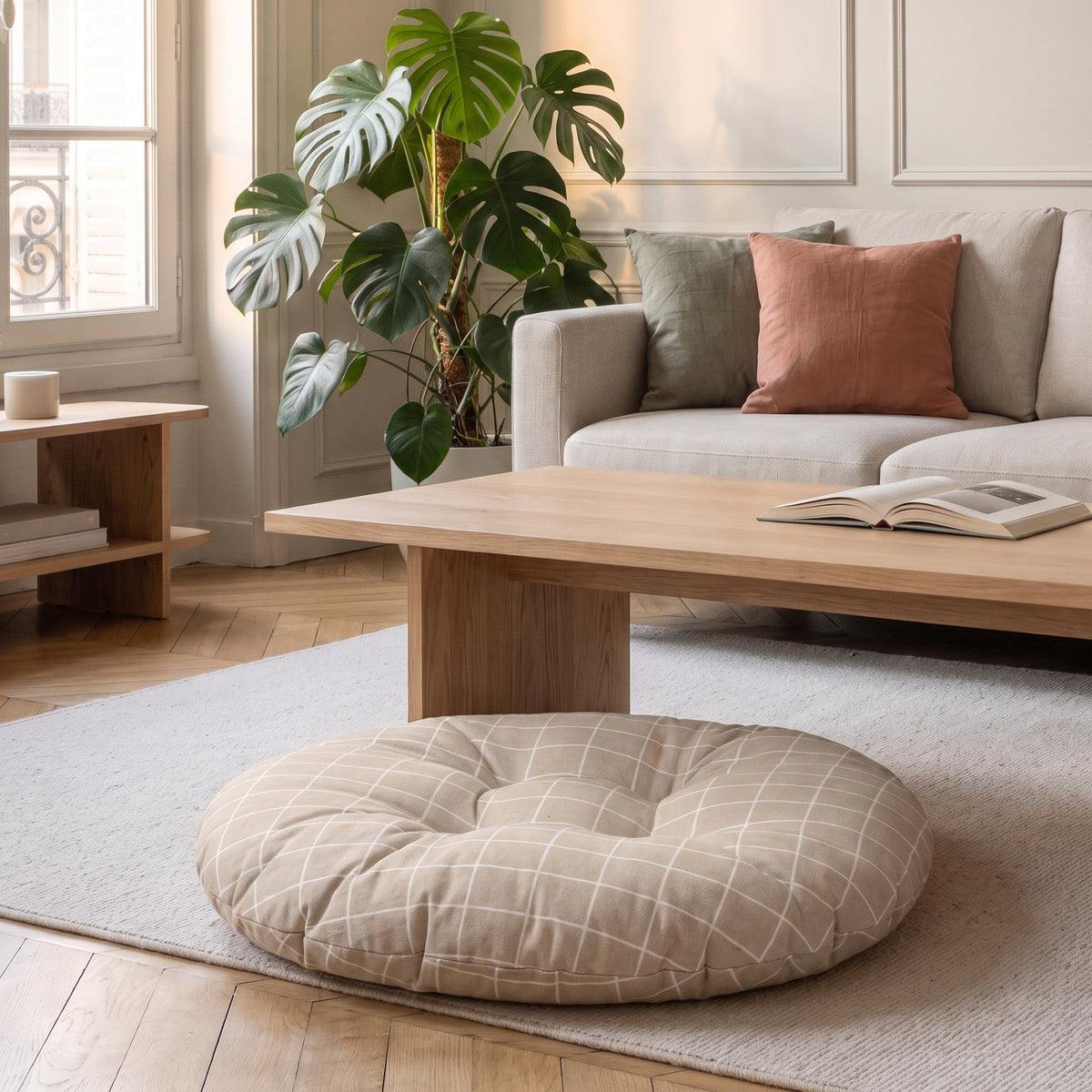 Coussin de sol rond à grands carreaux greige, posé sur un tapis devant un canapé