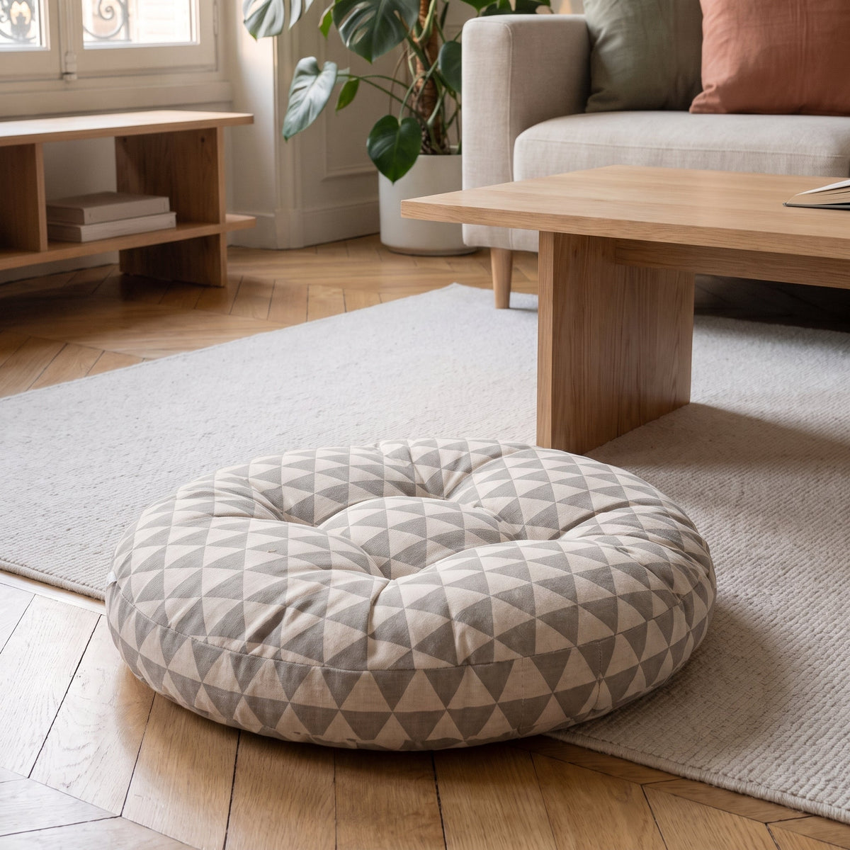 Coussin de sol rond à triangles gris sur fond écru, posé au sol près d'une table basse