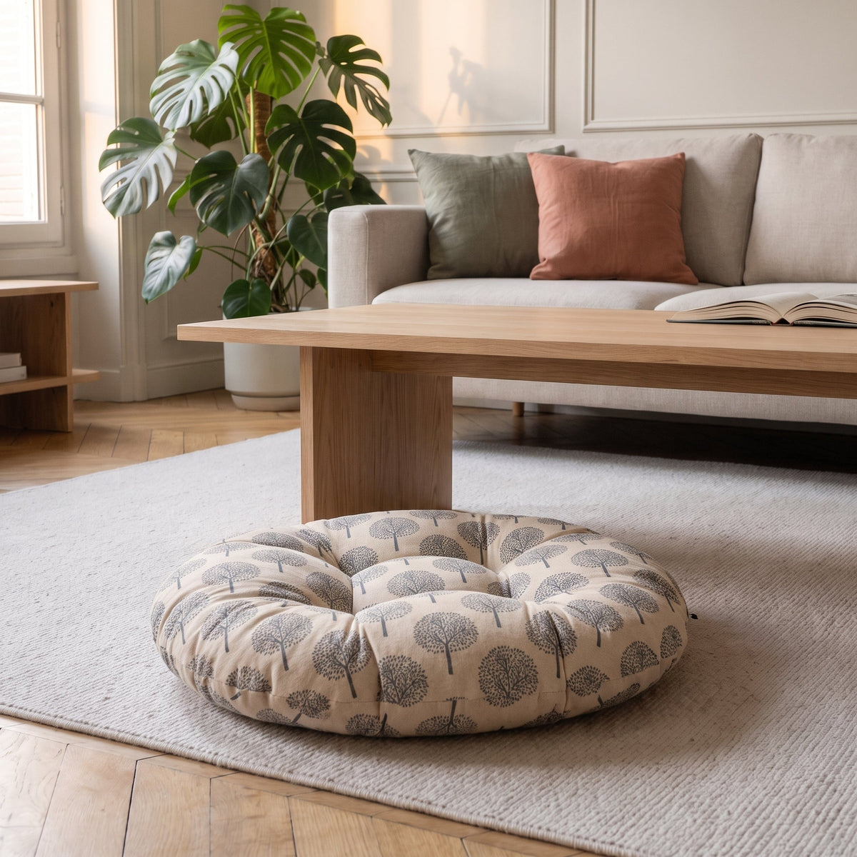 Coussin de sol rond imprimé arbres sur fond écru, posé sur un tapis clair