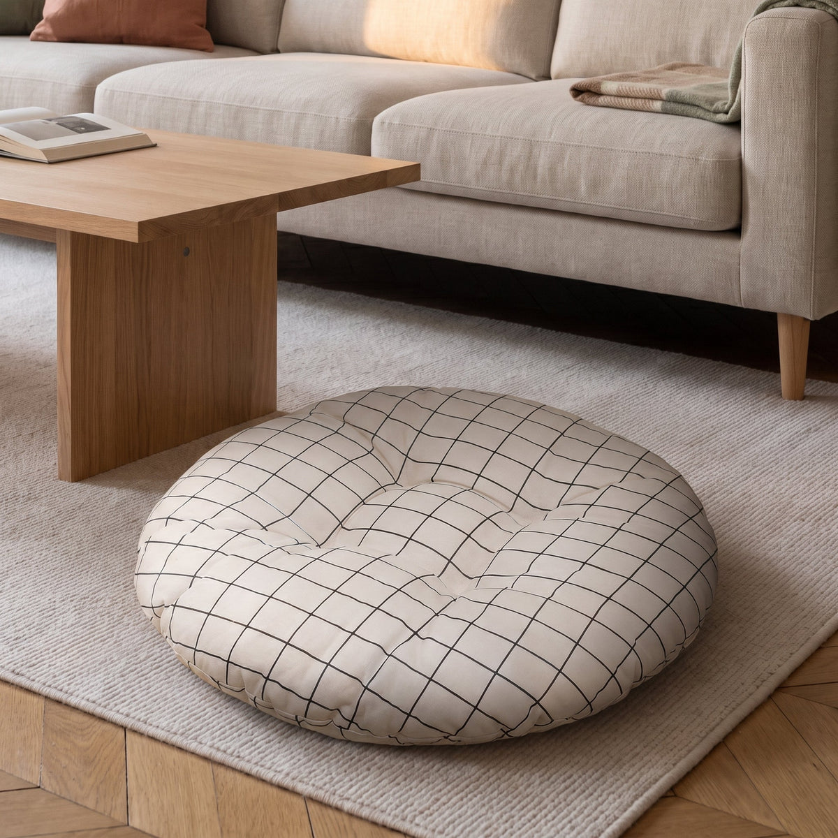 Coussin de sol rond à quadrillage noir sur fond écru, posé au sol dans un salon