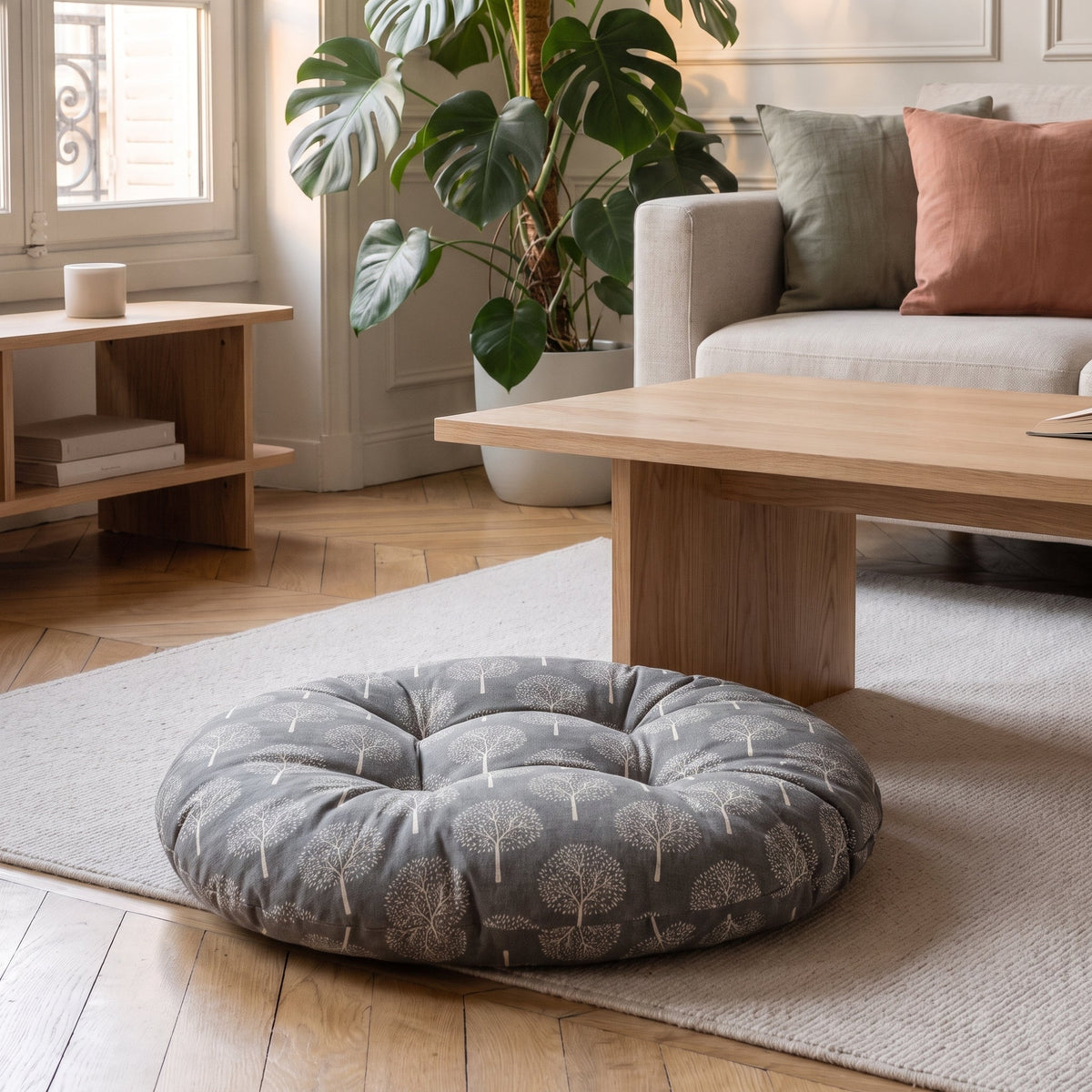 Coussin de sol rond imprimé arbres blancs sur fond gris ardoise, posé sur un tapis