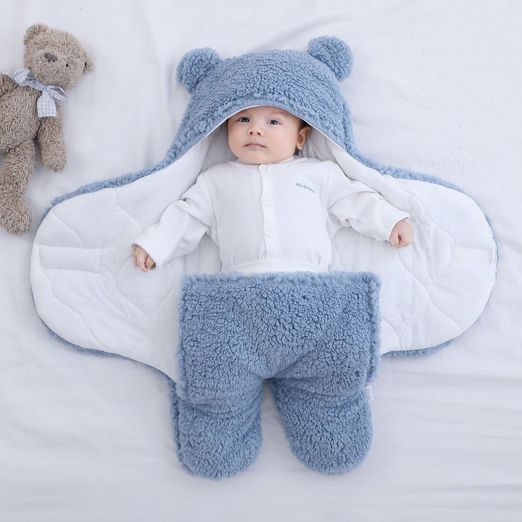 La gigoteuse bleue ouverte a plat, un bebe couche au milieu sur la doublure en coton matelasse blanc : on voit les deux pans ecartes, la bordure bleue qui fait le tour et les deux poches de jambes en bas