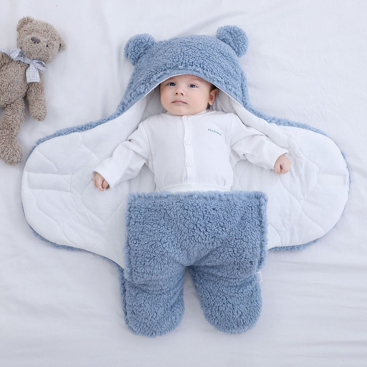 La gigoteuse bleue ouverte a plat, un bebe couche au milieu sur la doublure en coton matelasse blanc : on voit les deux pans ecartes, la bordure bleue qui fait le tour et les deux poches de jambes en bas