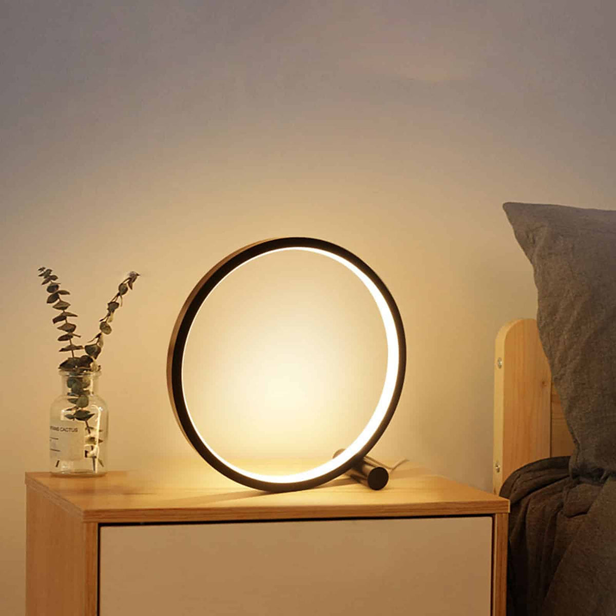 Lampe de table LED circulaire noire allumee sur une table de chevet