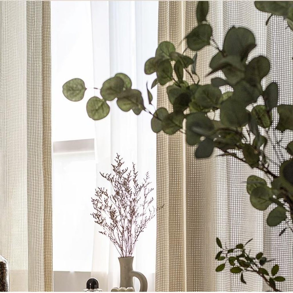 Rideau léger beige en maille devant la fenêtre, avec eucalyptus