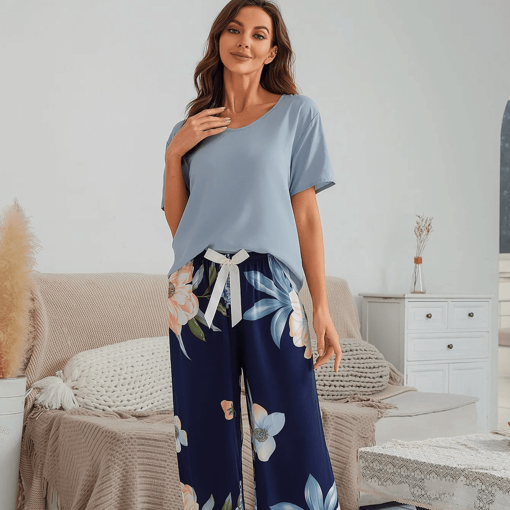 Pyjama femme, haut bleu ciel et pantalon large magnolias marine, debout dans une chambre claire, la main sur la poitrine.