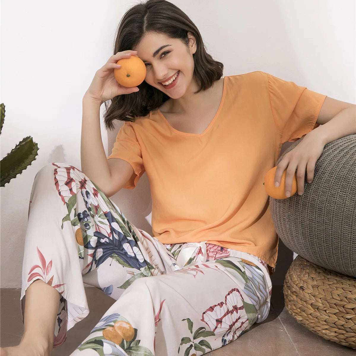 Pyjama femme, haut abricot et pantalon large fruits écru, assise au sol, la jambe tendue qui déploie toute la largeur du bas.