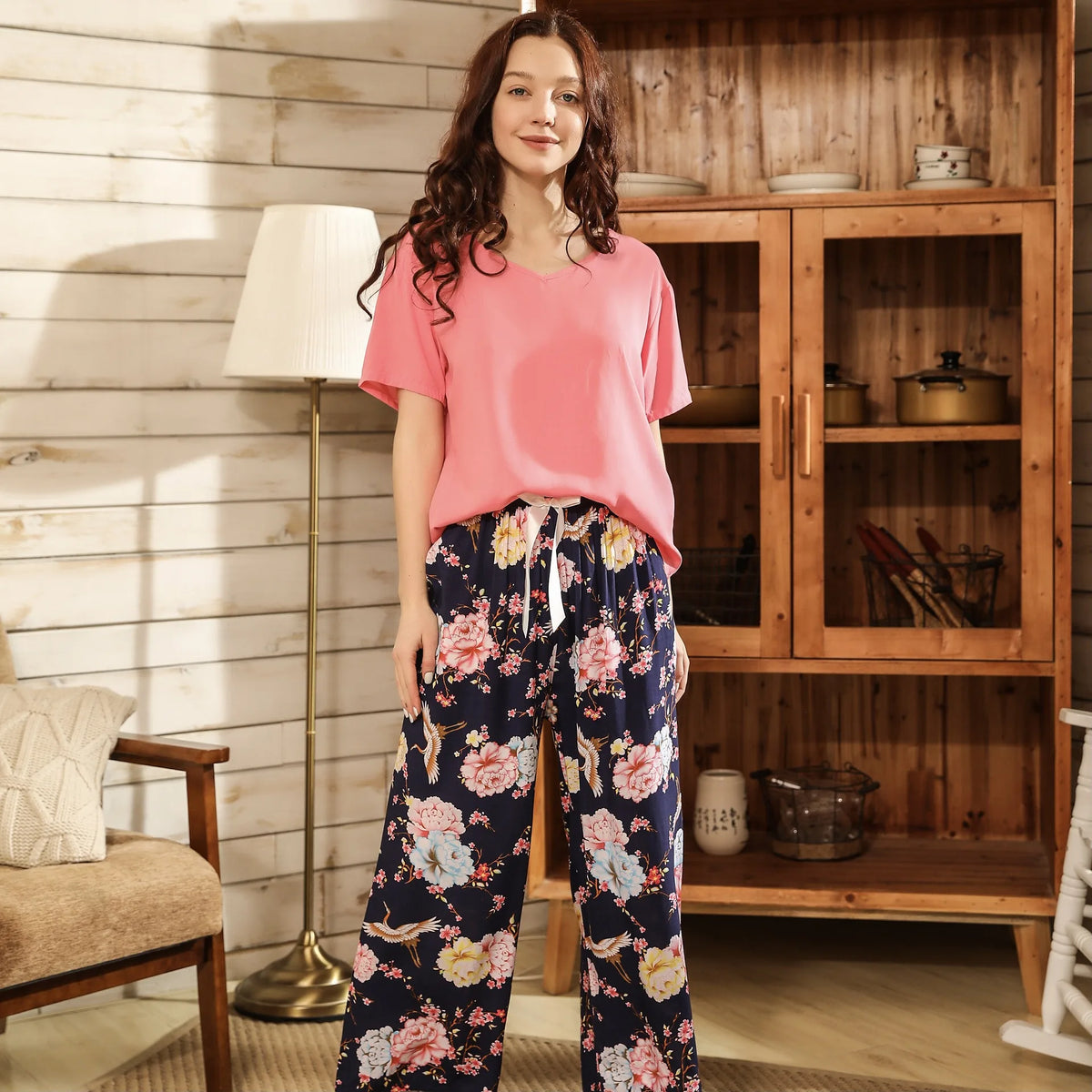 Pyjama femme, haut corail et pantalon large pivoines marine, debout dans un salon en bois, de face.
