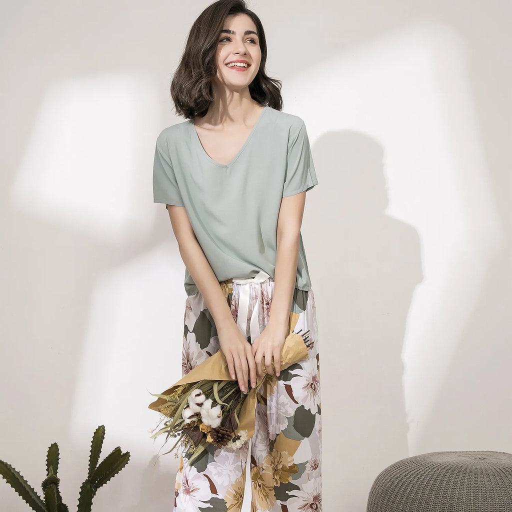Pyjama femme, haut sauge et pantalon large grandes fleurs écru, debout, un bouquet de fleurs séchées dans les mains.