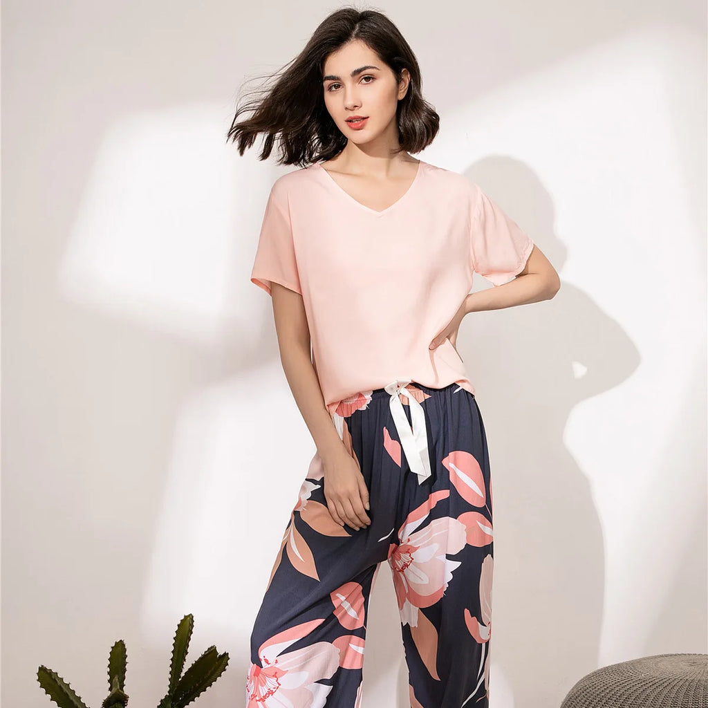Pyjama femme, haut rose et pantalon large magnolias marine, portés debout devant un mur clair.