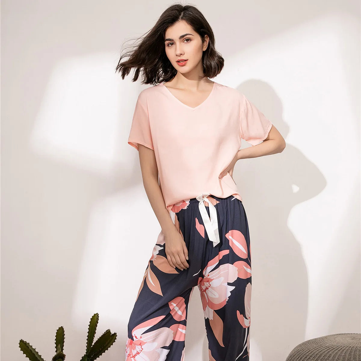 Pyjama femme, haut rose et pantalon large magnolias marine, portés debout devant un mur clair.