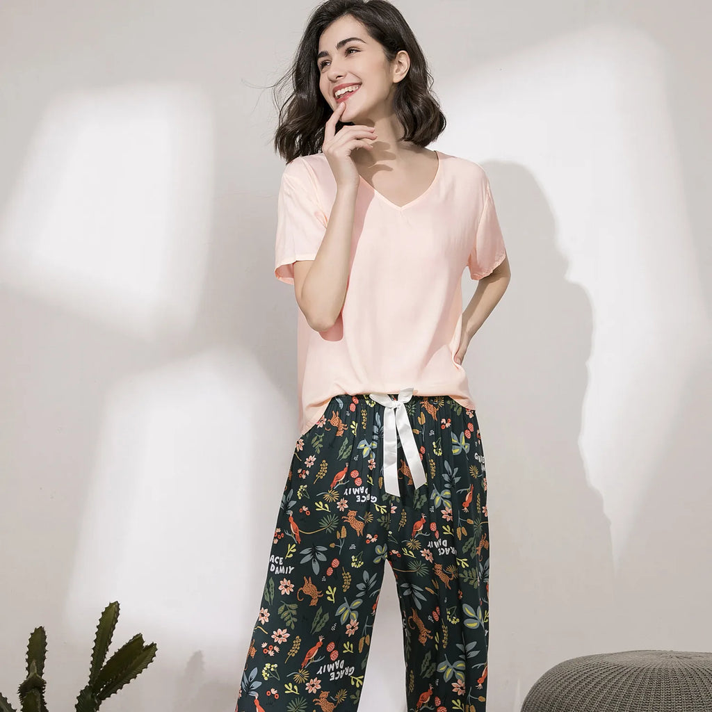 Pyjama femme, haut rose et pantalon large jardin vert forêt, portés debout devant un mur clair.
