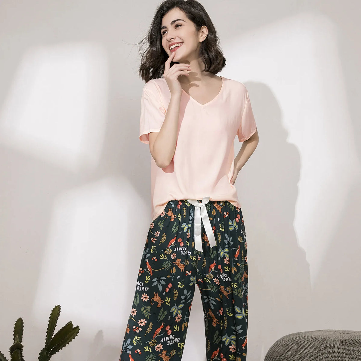 Pyjama femme, haut rose et pantalon large jardin vert forêt, portés debout devant un mur clair.