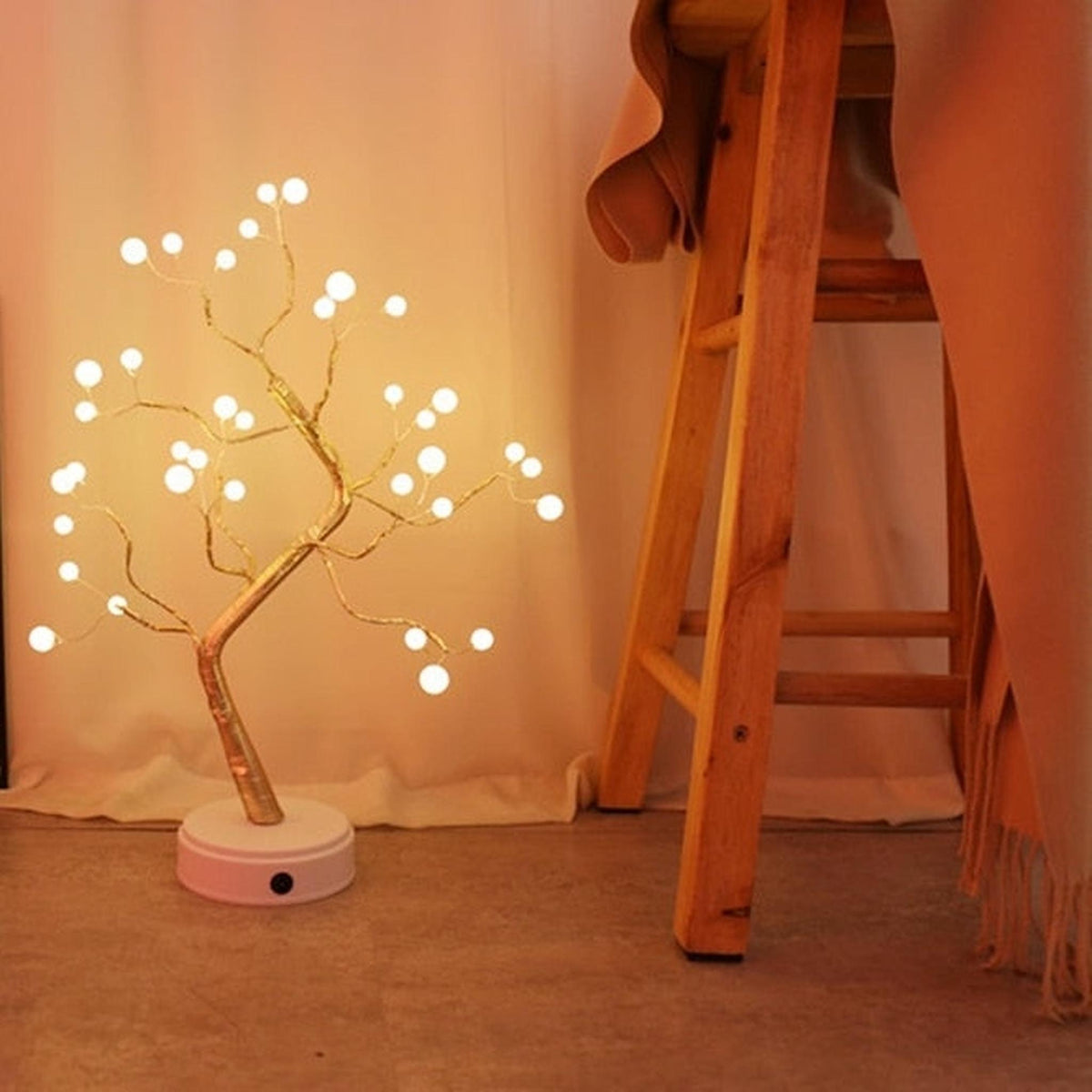 Arbre lumineux en fil de cuivre au sol près d'un escabeau en bois