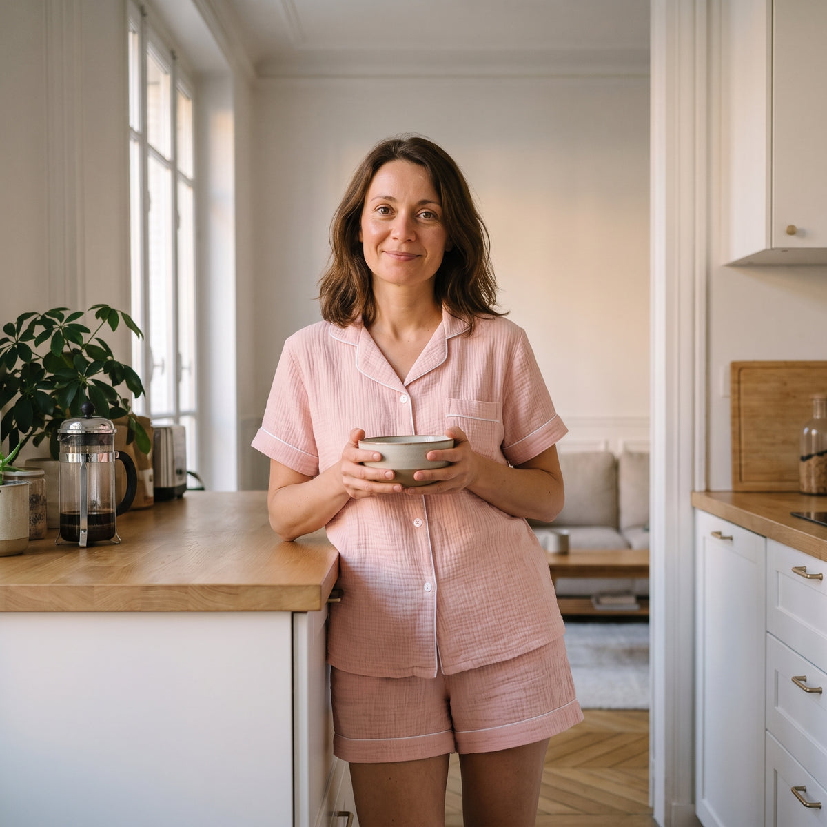 Femme en pyjama rose poudré, un bol à la main, dans sa cuisine le dimanche matin Image