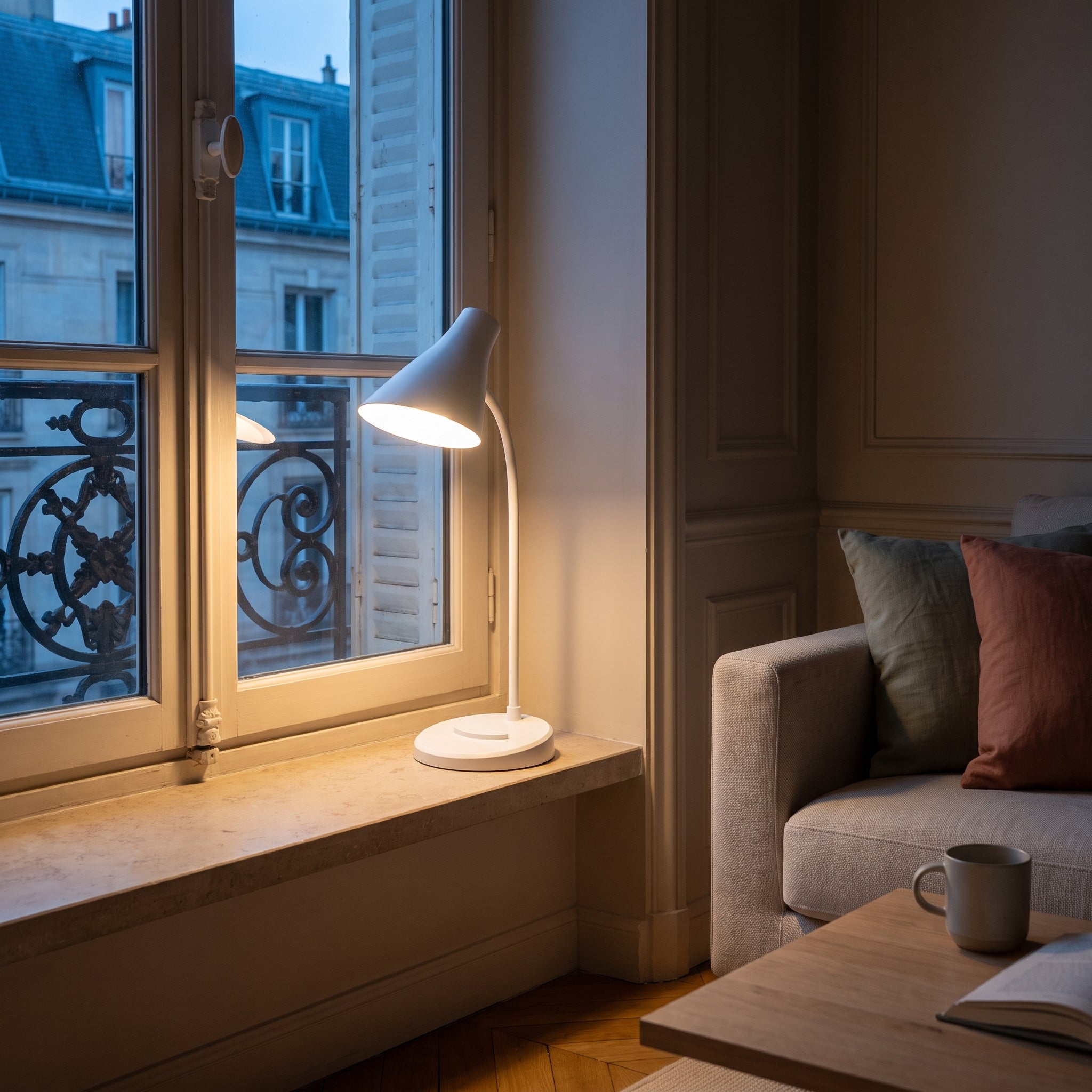 La lampe blanche allumée sur le rebord de pierre d'une fenêtre haussmannienne, au bleu de la fin du jour, seule source de lumière du coin salon. Image