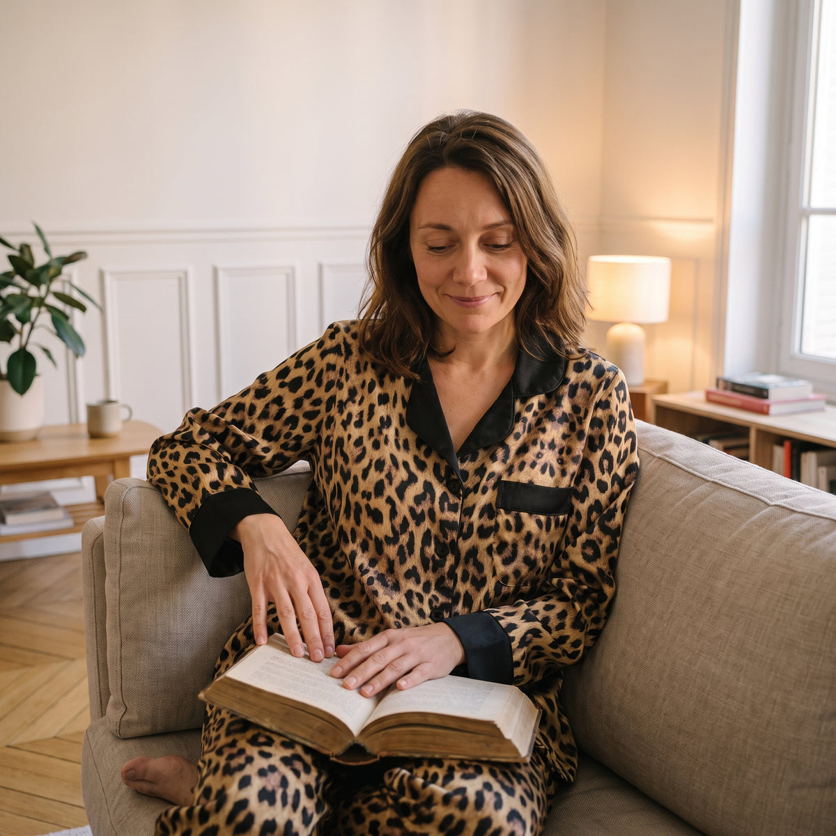 Femme assise sur son canapé avec un livre, en pyjama en satin imprimé léopard Image