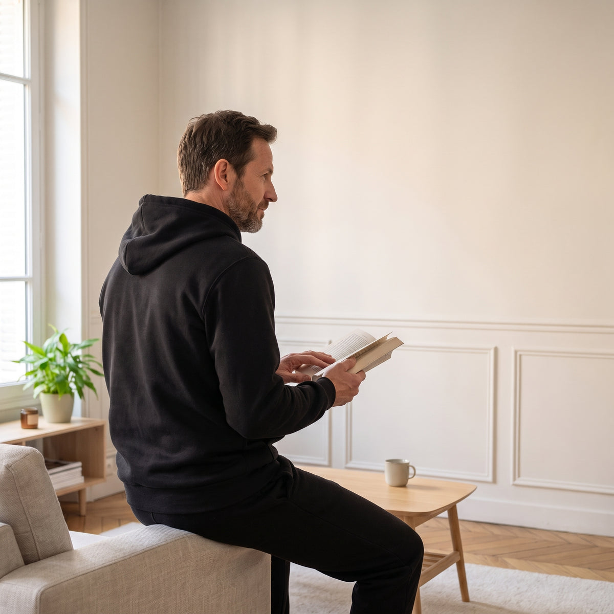 Homme en ensemble jogging noir, de dos, un livre ouvert sur son canapé Image