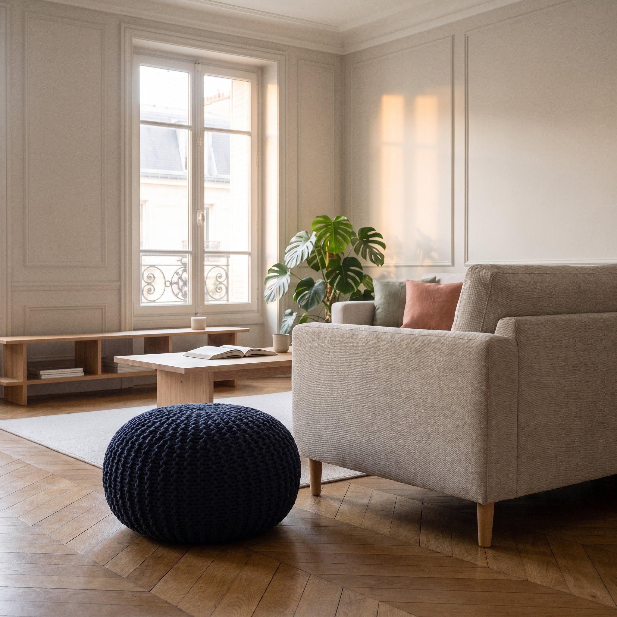 Pouf rond bleu marine posé sur le parquet à côté d'un canapé en tissu clair, son sommet arrivant plus bas que l'assise Image