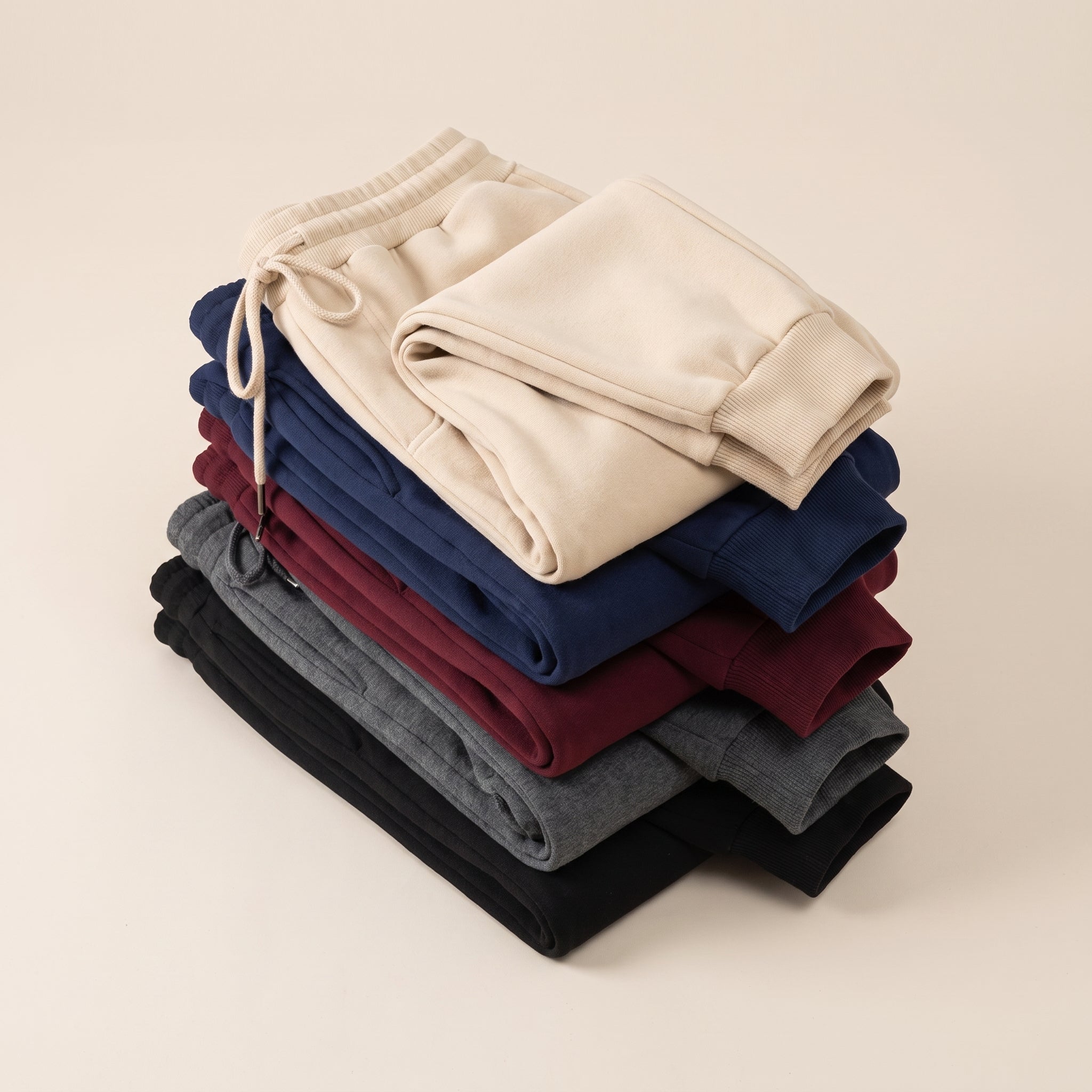 Cinq pantalons de jogging pliés en pile, du beige au noir Image