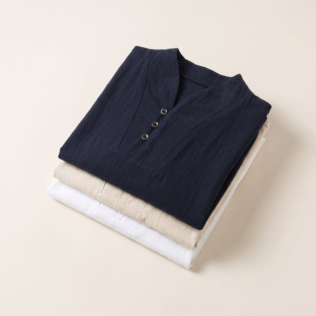 Trois ensembles en coton et lin pliés en pile, blanc, écru et bleu marine Image