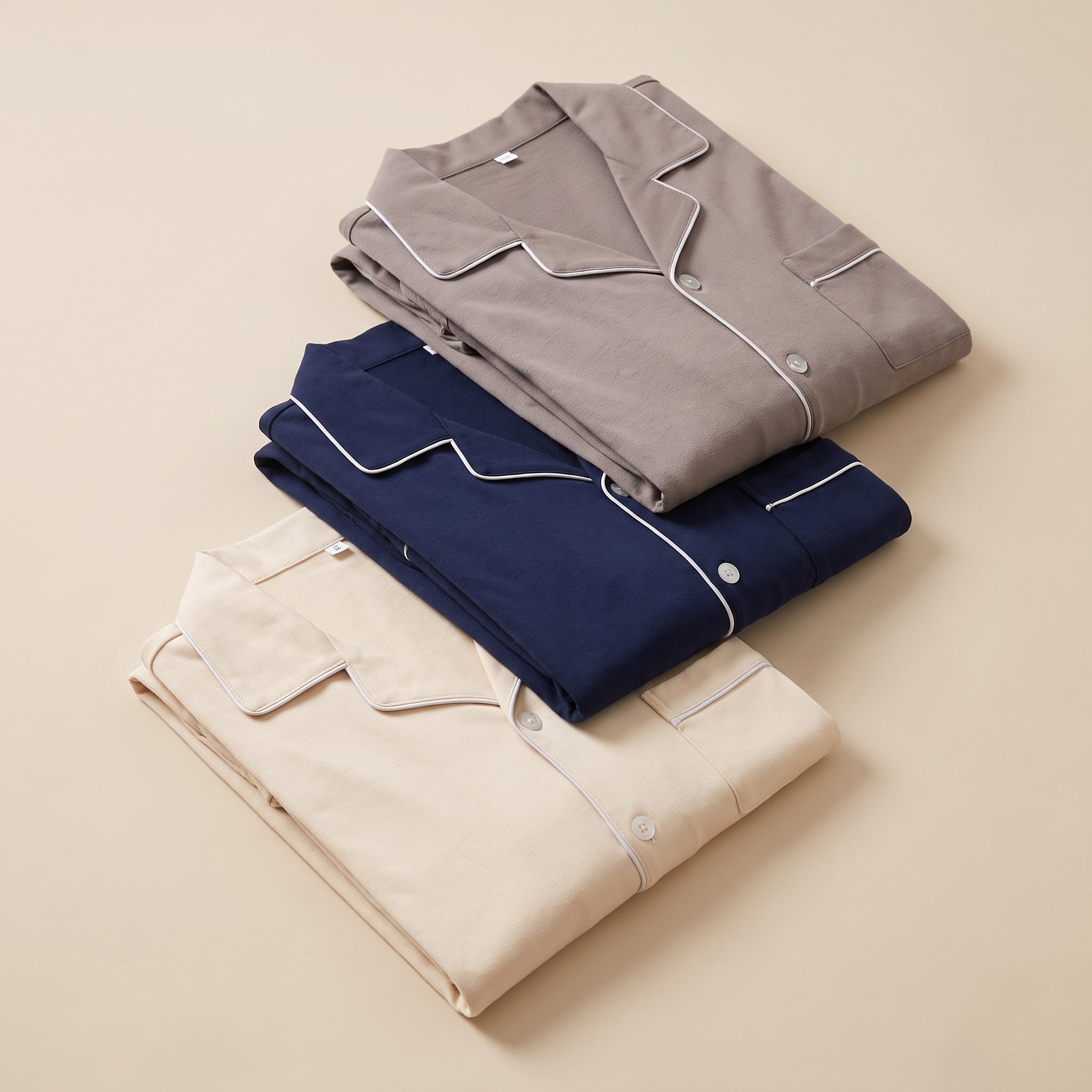 Trois pyjamas en coton uni pliés en pile, beige, bleu marine et taupe Image