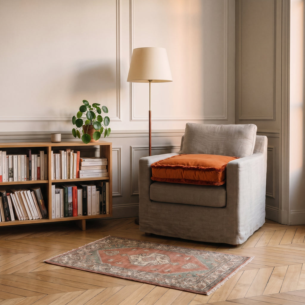 Coussin de sol en velours terracotta posé sur l'assise d'un fauteuil
