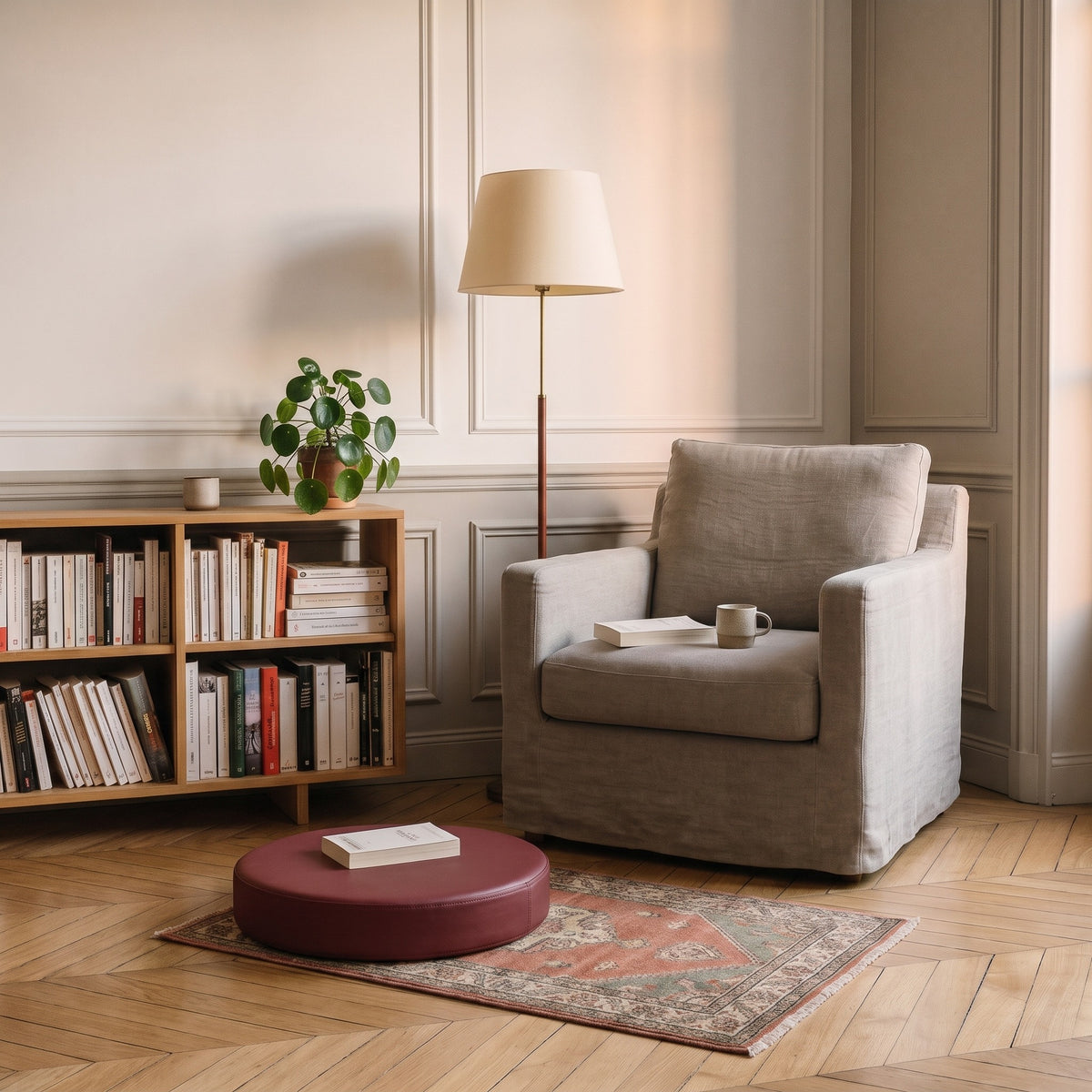 Coussin de sol rond bordeaux posé sur le tapis d'un coin lecture devant un fauteuil en lin, un livre fermé posé dessus