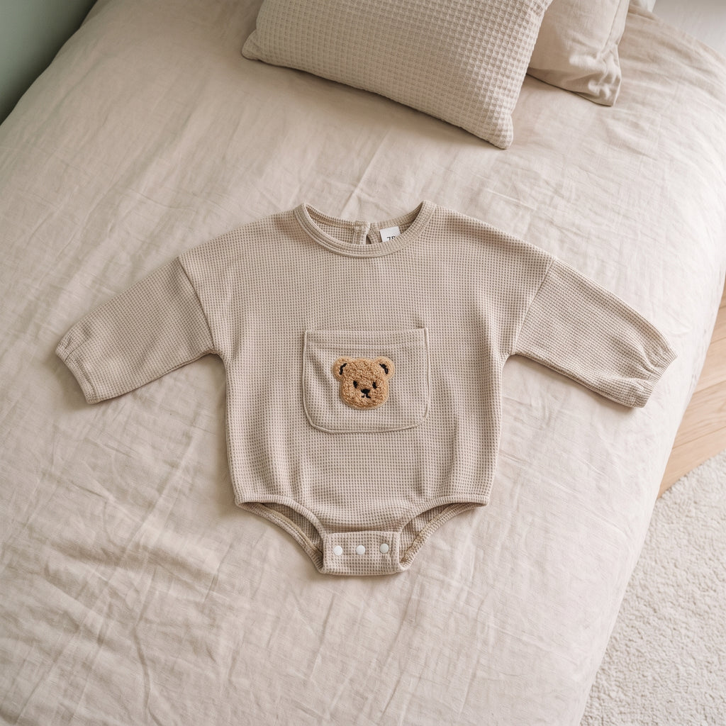 Barboteuse bébé beige vue du dessus, manches bouffantes et pressions sous l'entrejambe