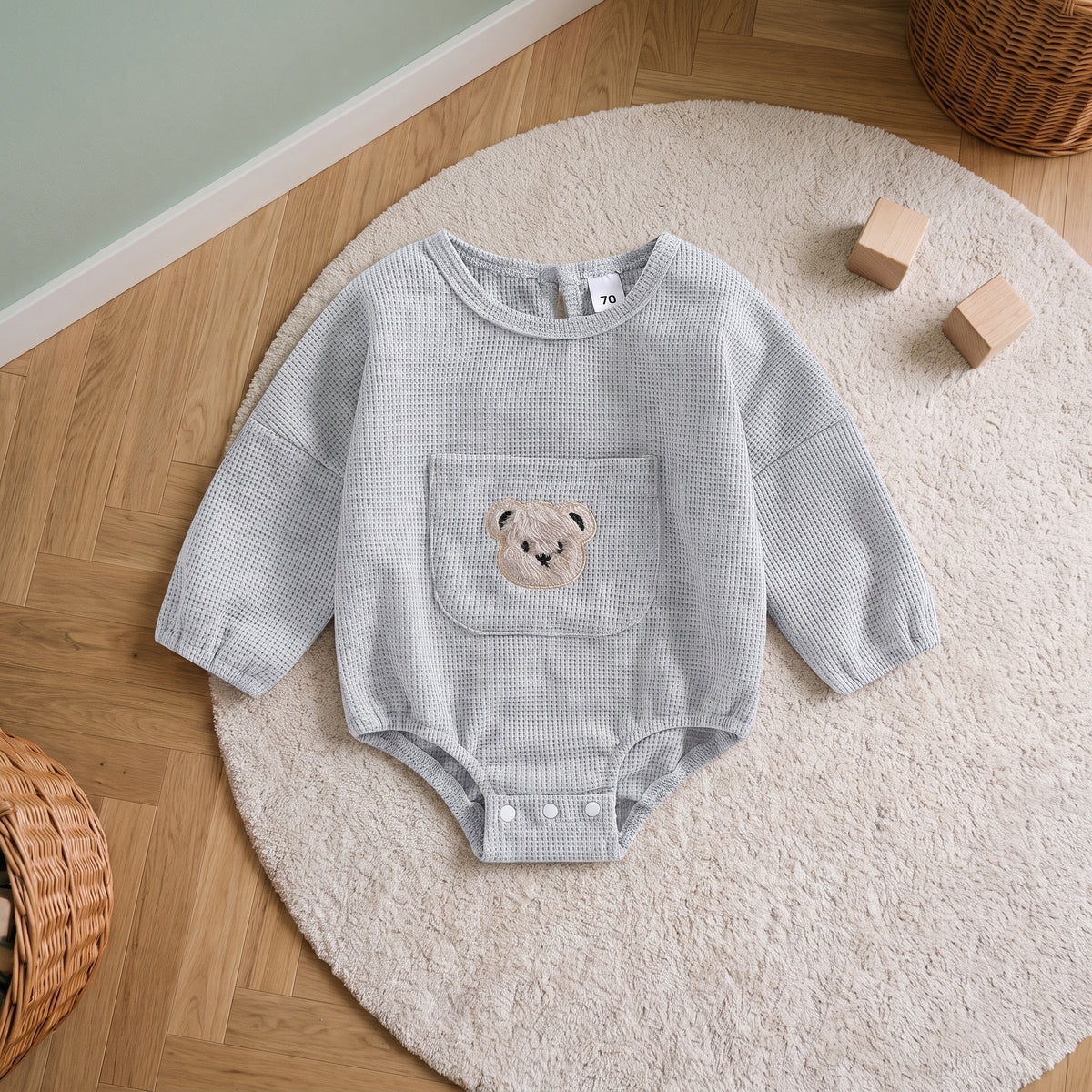 Barboteuse bébé grise en maille gaufrée, posée sur un tapis rond crème